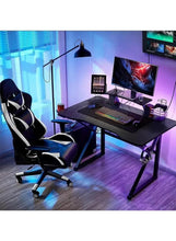 Ergonomic gaming office chair in black with white trim, beside desk setup