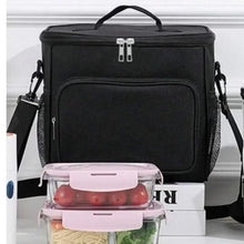 Black lunch box with shoulder strap, front pocket panel and zipper top; food container shown.