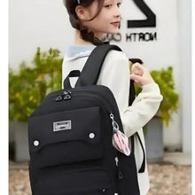 Black school backpack with front flap pocket, side zipper, and pink keychain charm.