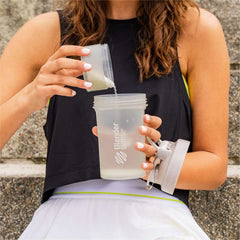 Woman pouring supplement from pill cup into BlenderBottle shaker bottle with pill organizer while seated