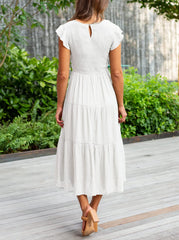 Back view of a woman wearing a white boho summer maxi dress women style in an outdoor garden setting