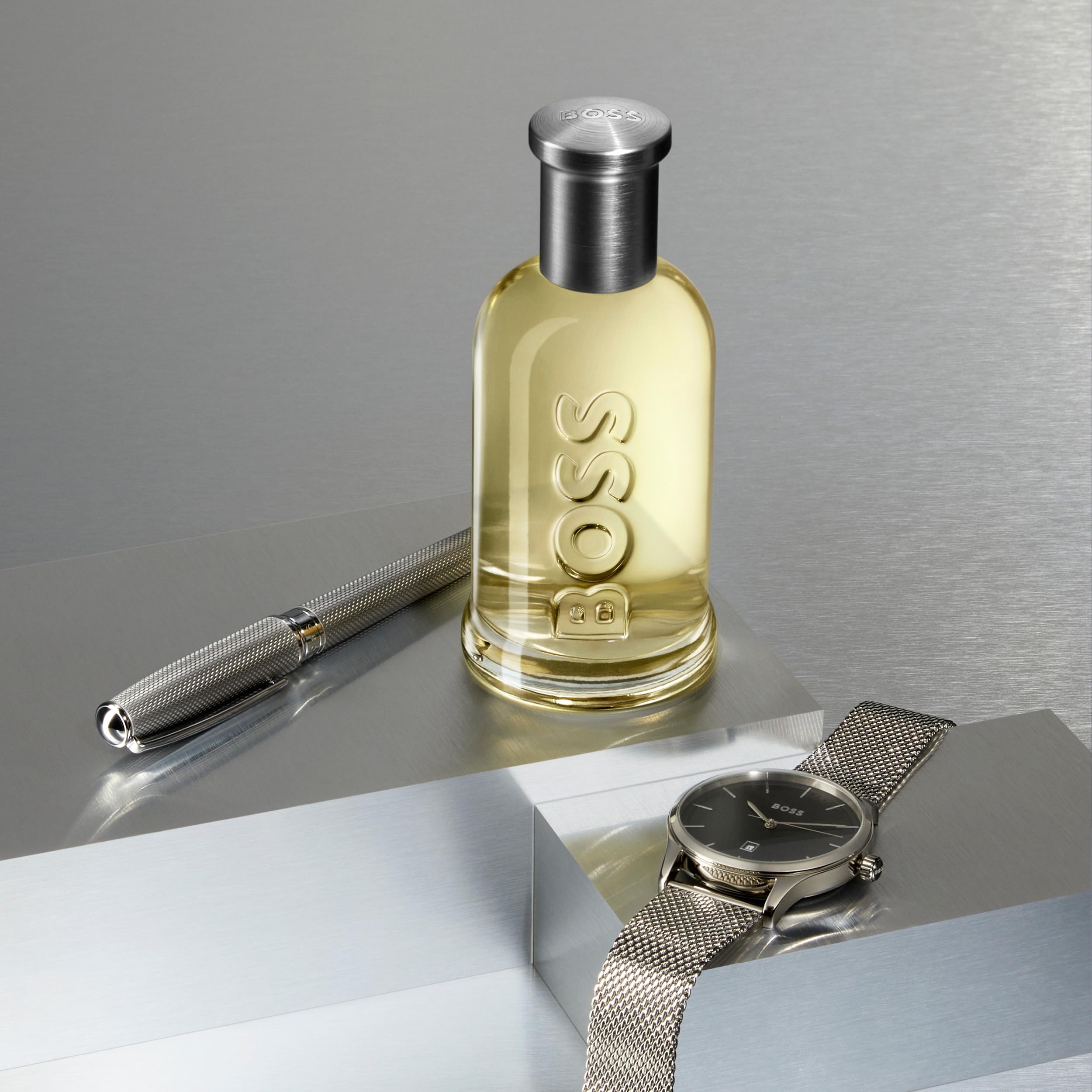 Boss Bottled Eau De Toilette for men by Mumzar displayed with a silver pen and wristwatch on a metallic surface