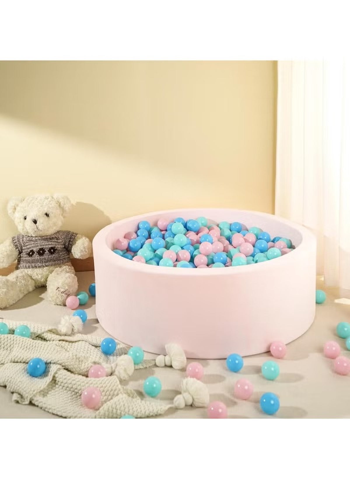 Huitich pink round play ball pit filled with BPA-free play ball pit balls in blue, pink, and teal colors with teddy bear and blanket nearby