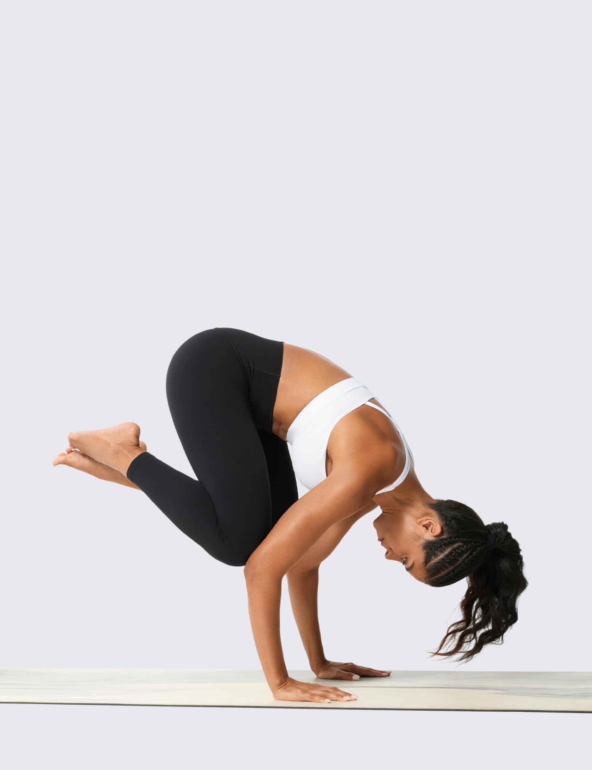 Woman wearing high waisted workout leggings and white sports bra doing a crow yoga pose