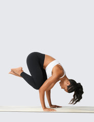 Woman wearing high waisted workout leggings and white sports bra doing a crow yoga pose
