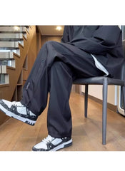 Huitich breathable outdoor pants for men in black worn with black and white sneakers sitting on chair indoors