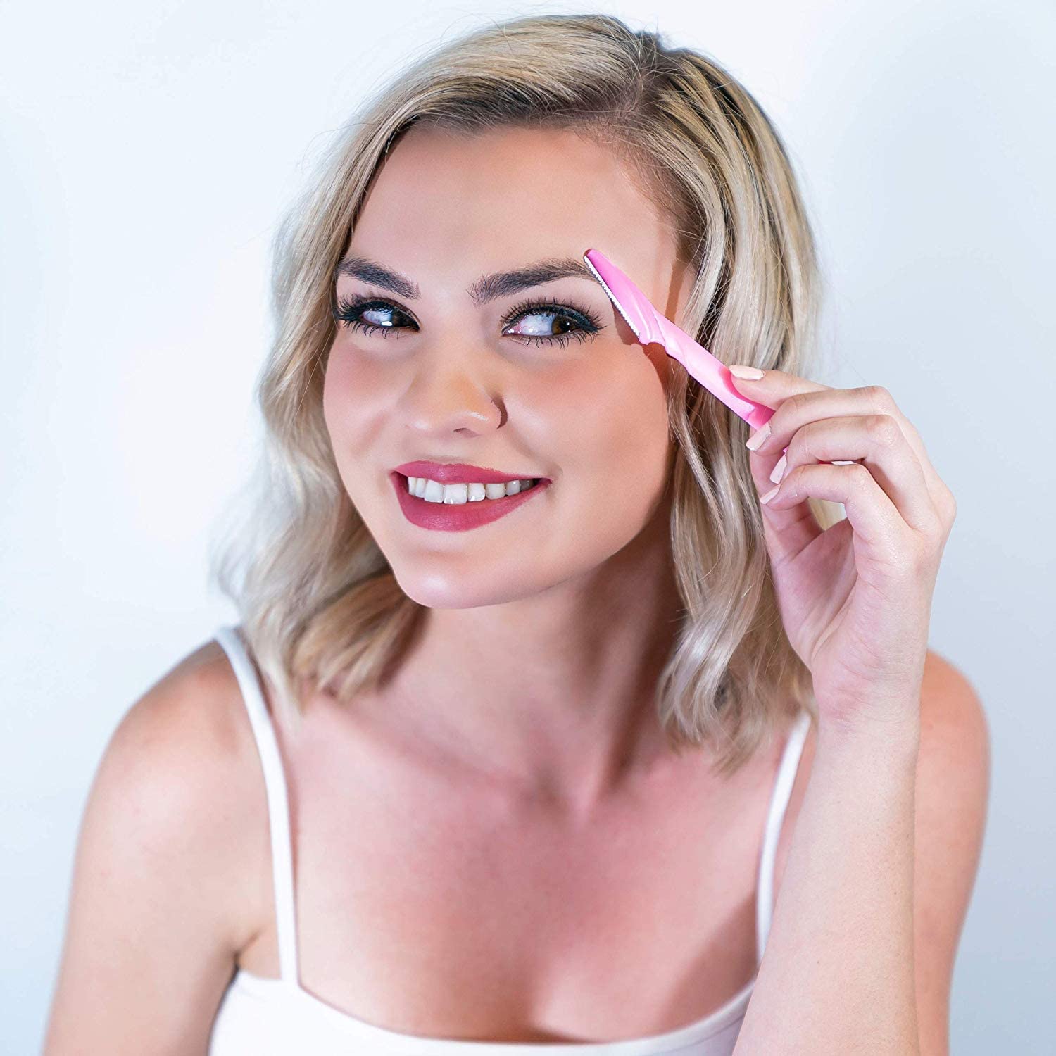 Blonde woman using a pink eyebrow razor for women and men to shape and remove fine facial hair