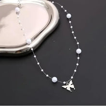 Close-up of silver pearl bead necklace with dangling butterfly charm at the clasp.