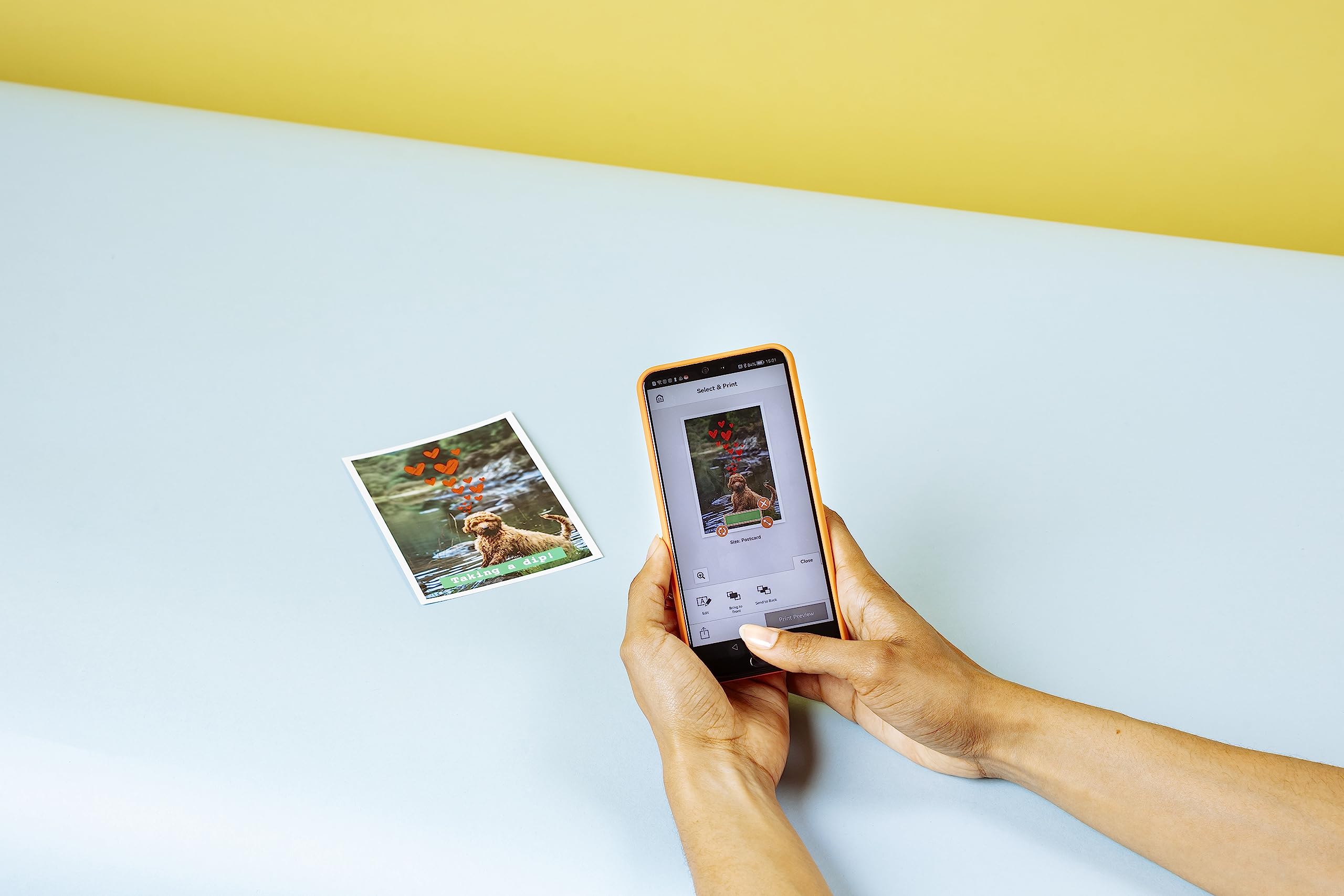 Person printing a photo on blue surface using Canon RP108 ink and paper set with smartphone