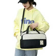 Diaper bag worn crossbody in cream dots and black with front teddy label