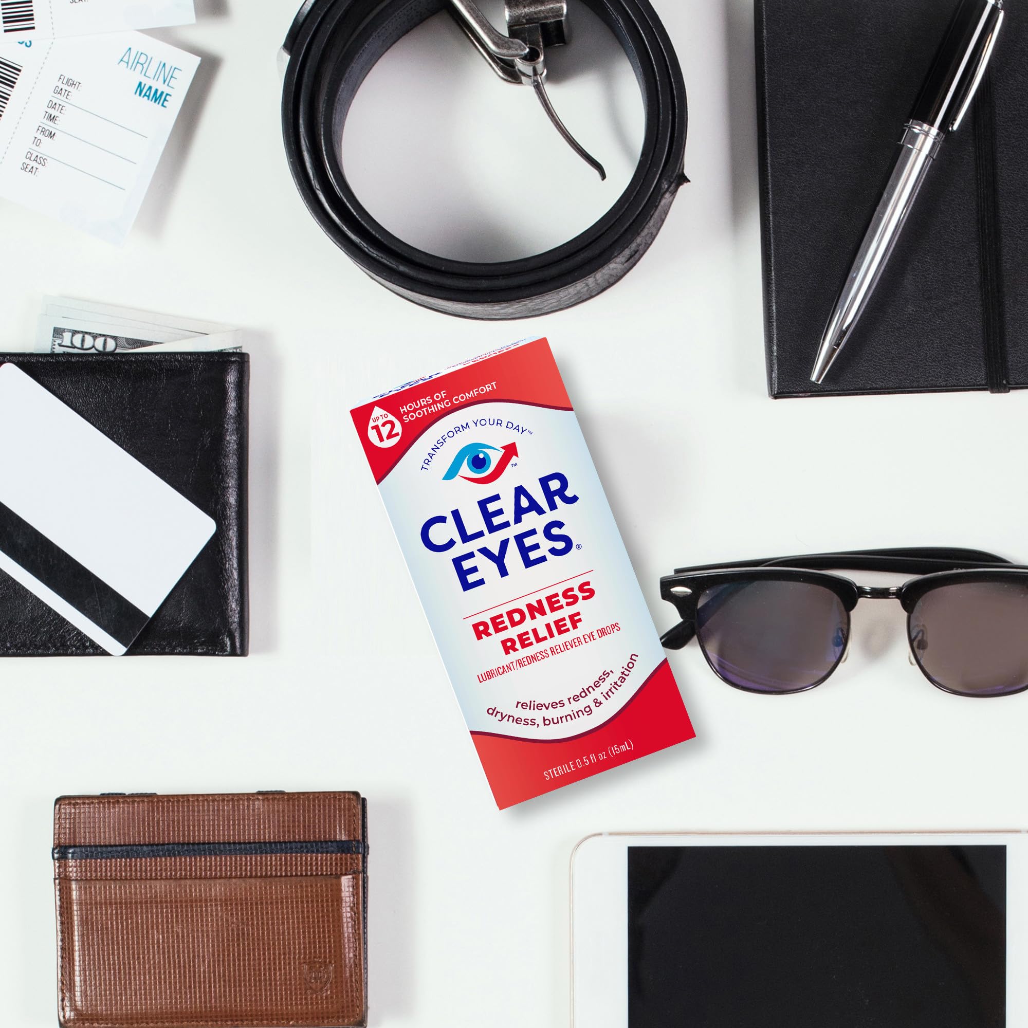 Clear Eyes redness relief eye drops box on a white desk beside sunglasses wallet belt and tablet
