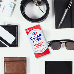 Clear Eyes redness relief eye drops box on a white desk beside sunglasses wallet belt and tablet