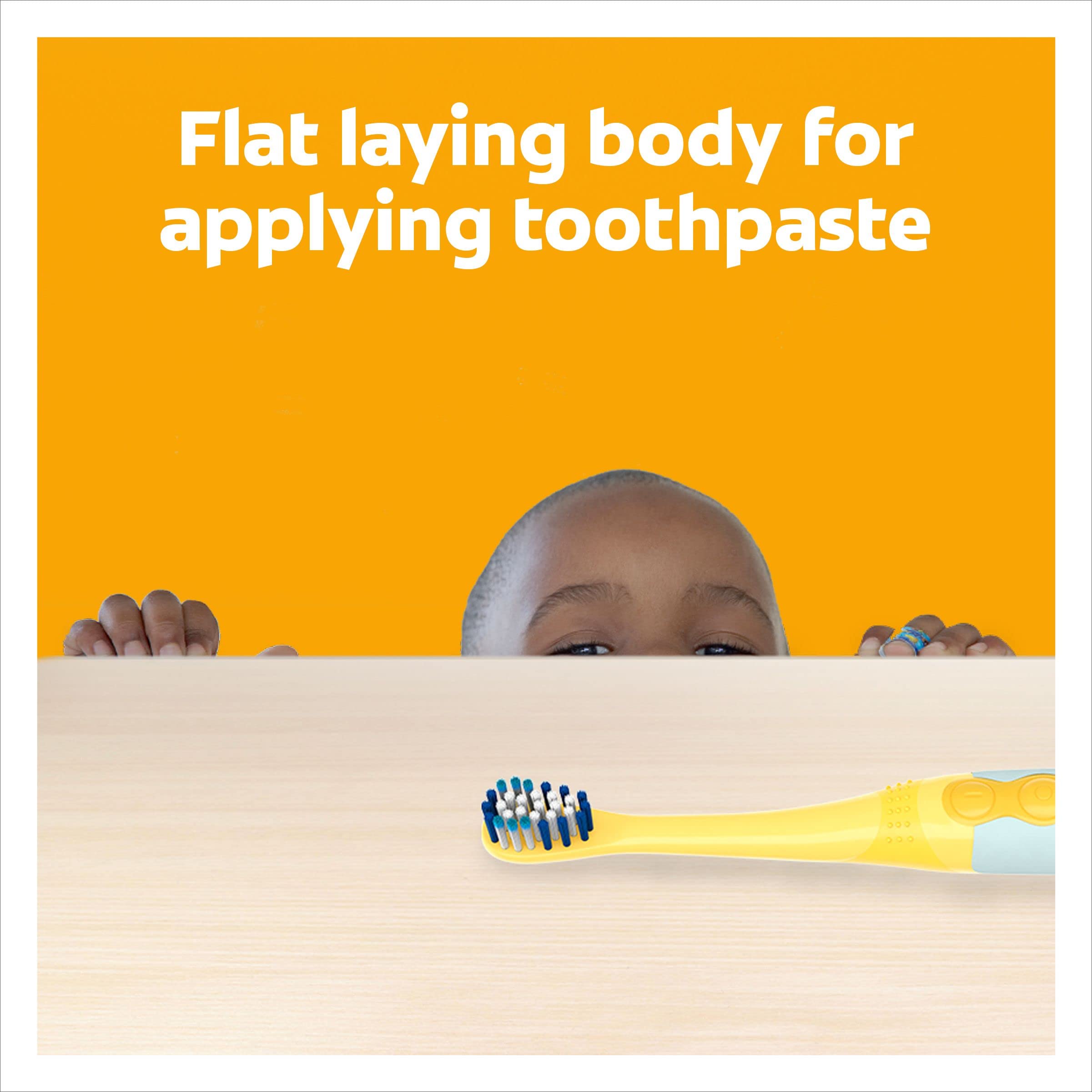 Colgate kids Minions toothbrush yellow brush with blue bristles lying flat on table and child peeking over edge