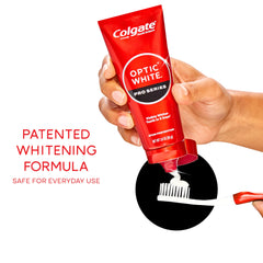 Hand holding Colgate optic white pro series toothpaste tube dispensing paste onto toothbrush illustrating whitening formula