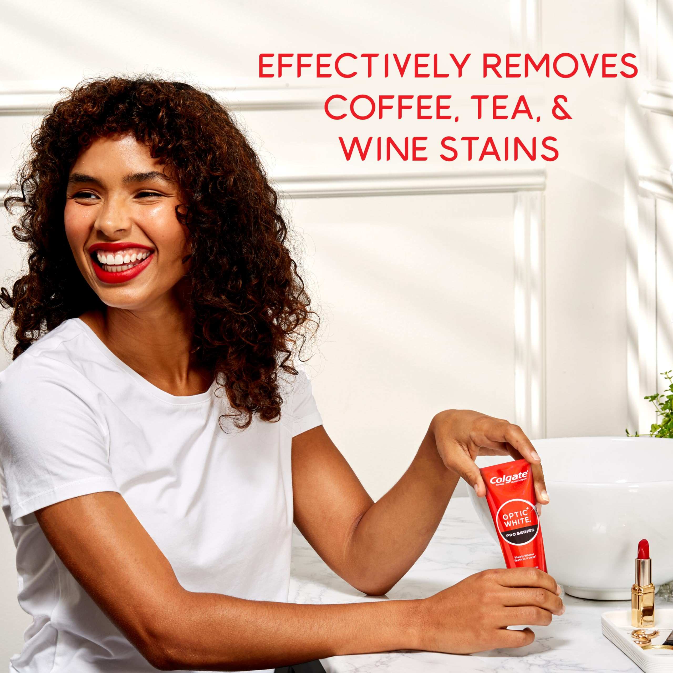 Smiling woman holding Colgate optic white pro series toothpaste tube at bathroom vanity removing coffee tea and wine stains