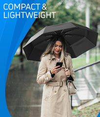 Rain-Mate compact travel umbrella in black used by woman in beige trench coat on rainy day