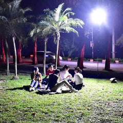 Group of people sitting on grass illuminated by a bright LED camping lantern 46W at night outdoors