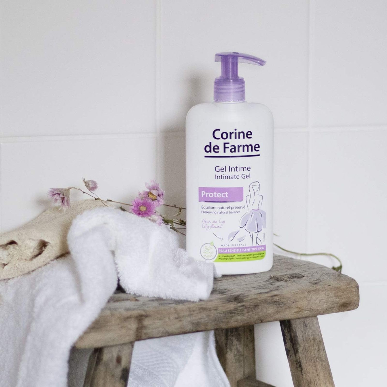 Corine de Farme intimate care gel pump bottle on wooden stool with white towel and pink flowers