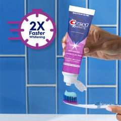 Hand squeezing Crest 3D White toothpaste tube onto toothbrush with blue gel and 2X faster whitening badge