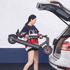 Woman folding and carrying Crony m365 aluminium scooter towards car trunk for easy transport