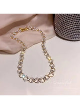 Crystal choker necklace with gold-tone chain and scattered round rhinestones, laid on fabric