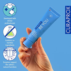 Hand holding Curaprox Be You gentle whitening toothpaste tube in blue packaging showing dental care benefits