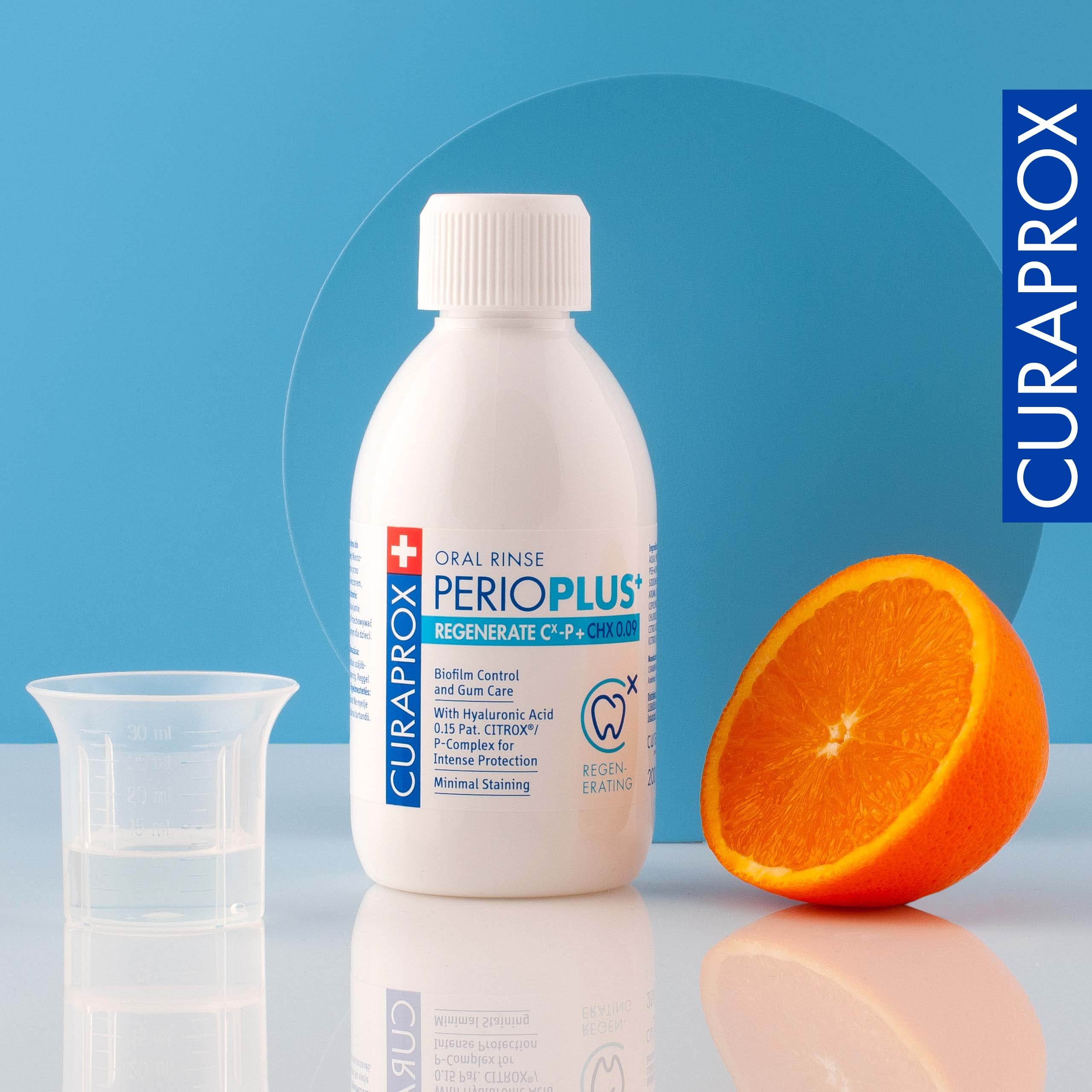 Curaprox Perio Plus Regenerate mouthwash bottle with measuring cup and sliced orange on blue background
