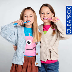 Two smiling girls brushing teeth with colorful toothbrushes promoting kids fluoride toothpaste strawberry flavor by Curaprox