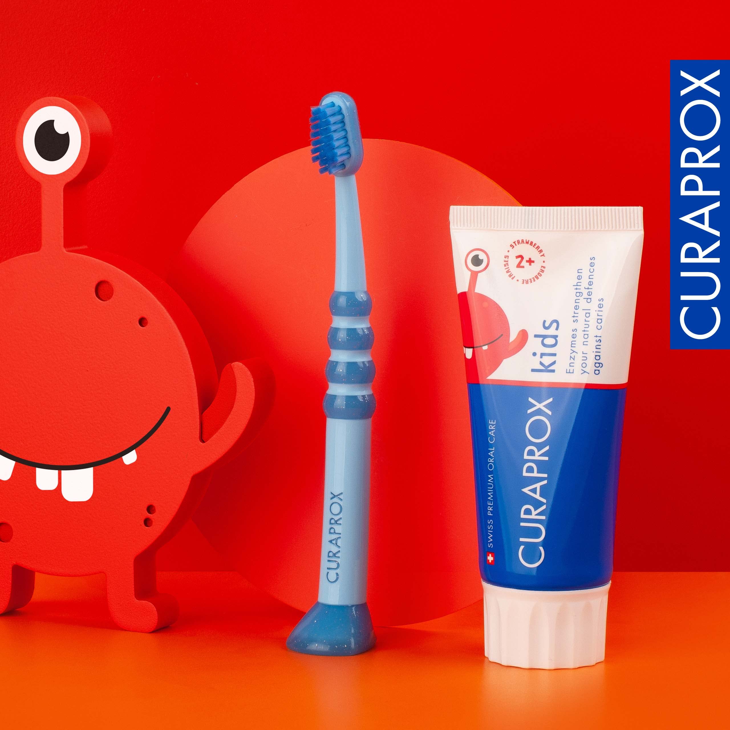 Curaprox kids fluoride toothpaste strawberry flavor tube with blue toothbrush and red monster toy