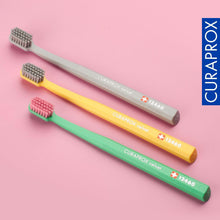 Three Curaprox CS 12460 toothbrushes, compact bristle heads on gray, yellow, green handles