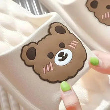 White plush slipper with smiling bear face patch on the vamp