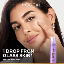L’Oréal Paris Revitalift Glass Skin liquid cream bottle beside model touching cheek
