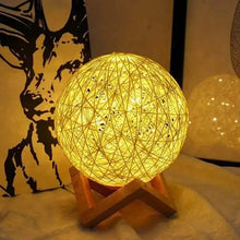 Decorative LED bedside lamp with glowing yellow rattan globe shade and wooden tripod stand
