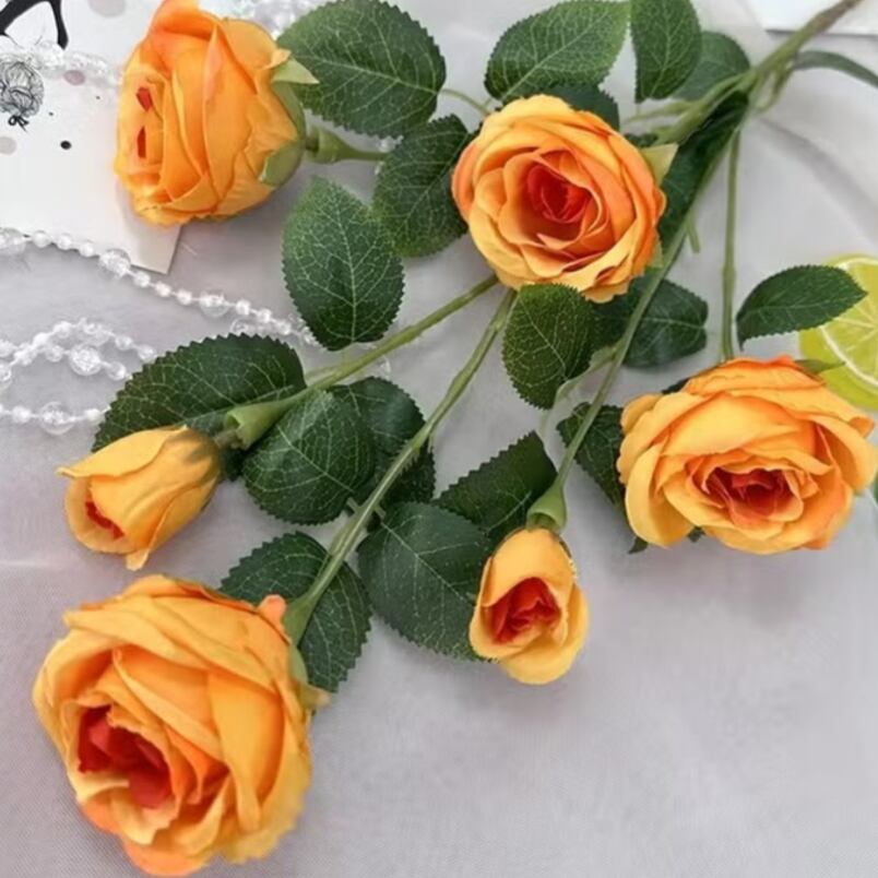 Huitich deep orange artificial roses with green leaves arranged on white surface