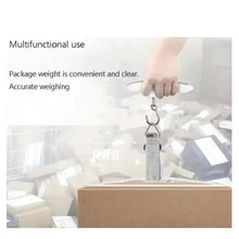 Portable digital luggage scale lifting a hanging strap above a cardboard box