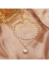Gold-tone double-layer pearl necklace laid flat, with round pearl pendant
