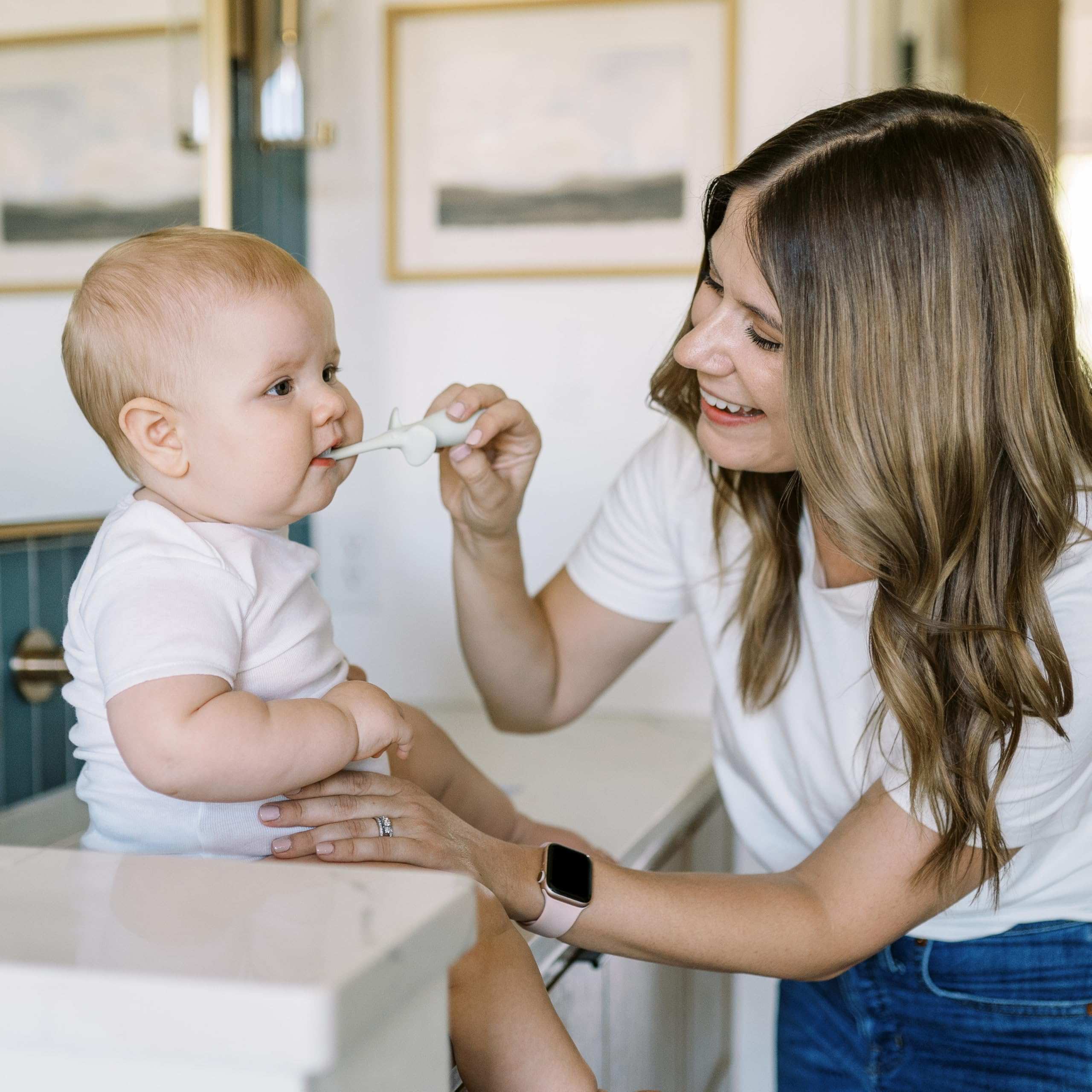 Mother using Dr Browns infant toothbrush 0-3 years to gently clean gums of smiling baby at home
