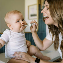 Parent brushing a baby’s teeth with a mint elephant toothbrush