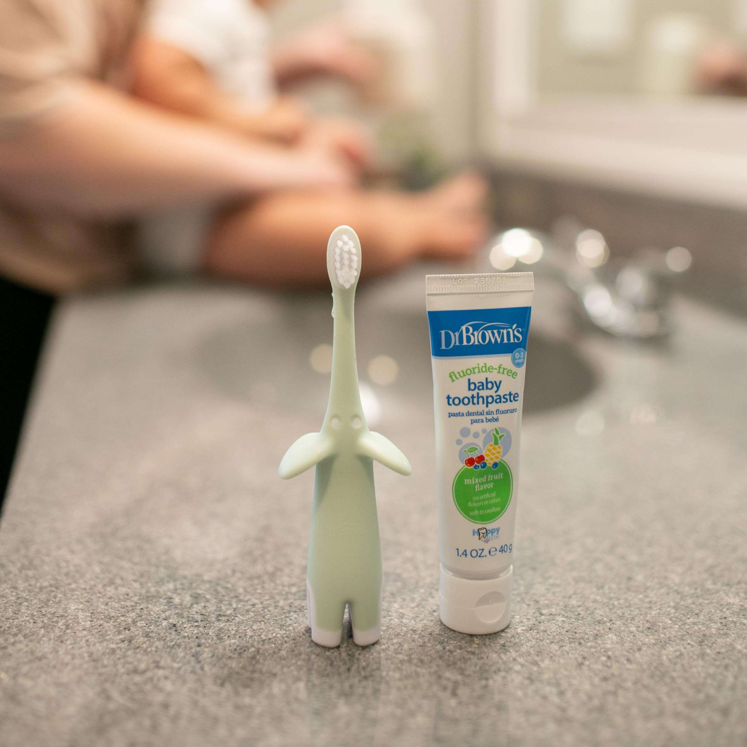 Dr Browns elephant baby toothbrush and baby toothpaste on sink with parent holding baby infant toothbrush 0-3 years