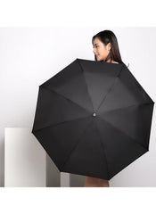Woman holding a black dual purpose automatic umbrella by Mumzar against a plain background