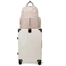 Light pink baby travel backpack mounted on a rolling suitcase with vertical front zips.