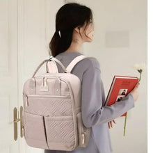 Light pink baby travel backpack worn on back with padded shoulder straps and front pocket.