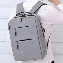 Gray laptop backpack held by person with front zipper and side carry handle.