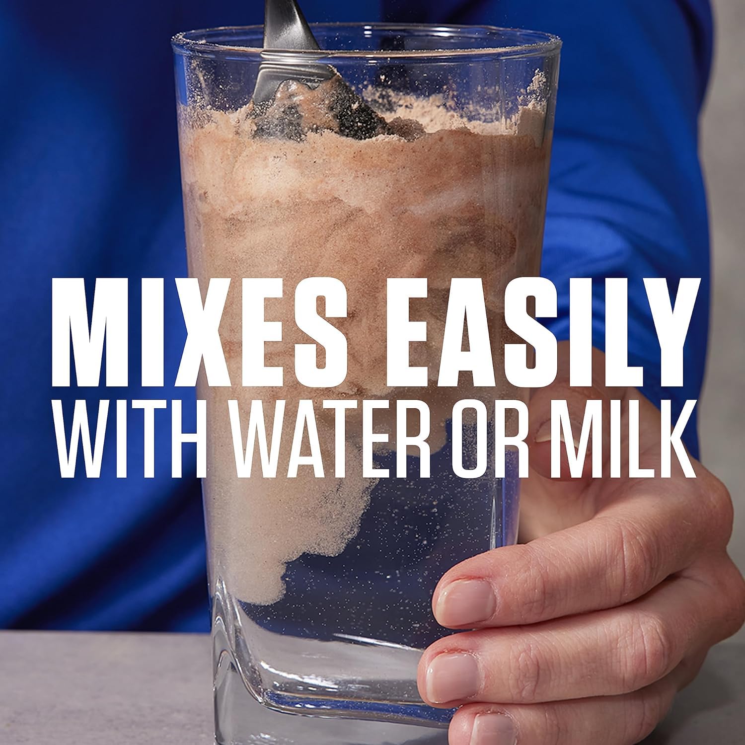 Dymatize Elite Whey Protein Rich Chocolate powder mixing in glass with spoon and hand showing it mixes easily with water or milk