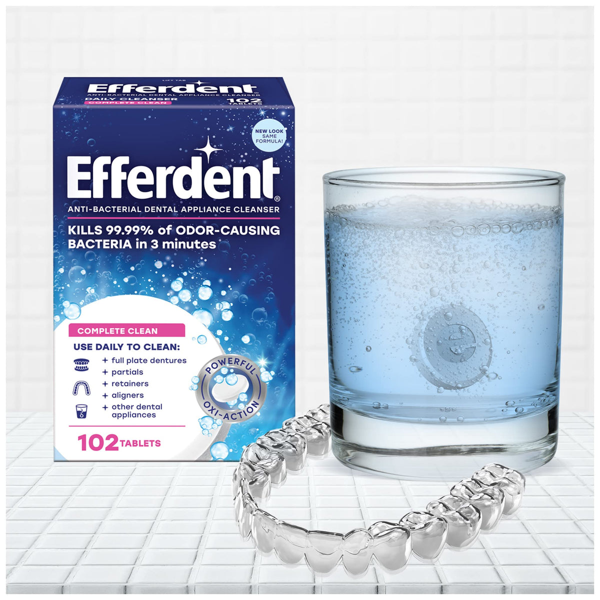 Box of Efferdent denture cleanser tablets beside a glass of bubbling solution and a clear denture appliance