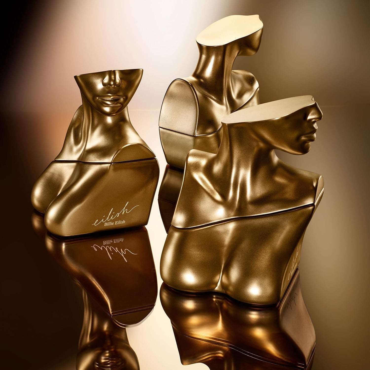 Sculptural golden bottles of Eilish Eau de Parfum for women by Billie Eilish Store on reflective surface