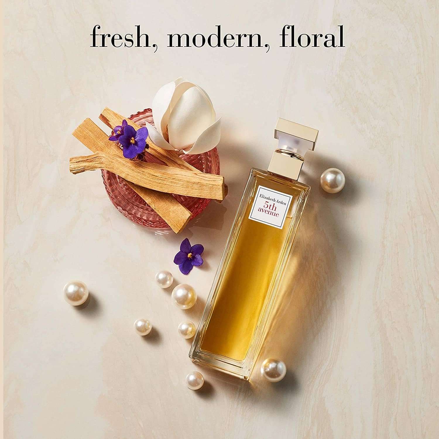 Elizabeth Arden 5th Avenue perfume bottle with fresh floral elements and pearls on a light background