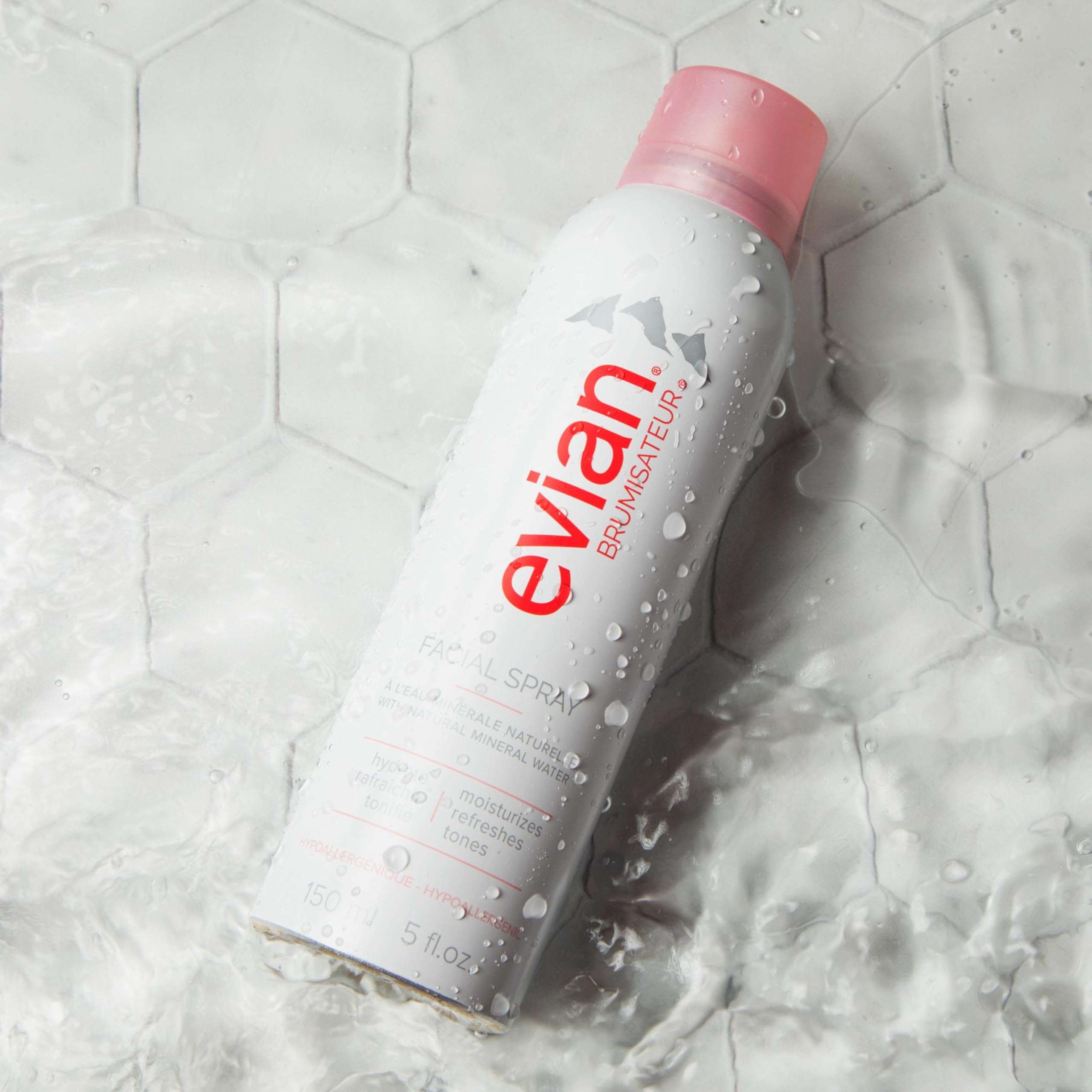 Evian facial spray 5 oz white bottle with pink cap surrounded by water droplets on tile surface