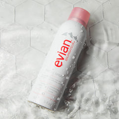 Evian facial spray 5 oz white bottle with pink cap surrounded by water droplets on tile surface