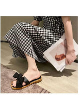 Black wedge sandals with oversized bow over open toe and tan-trimmed outsole